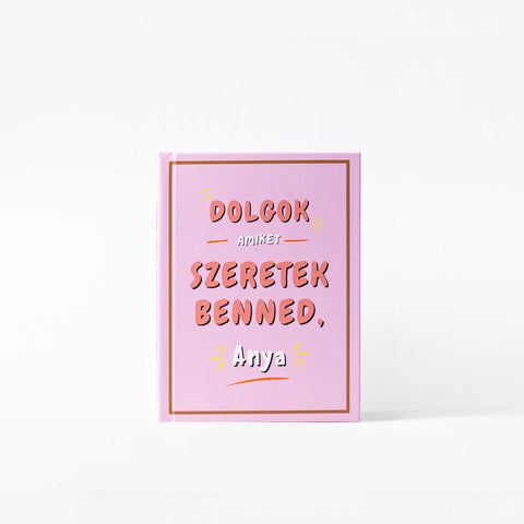 Rózsaszín ajándékkönyv, rajta a felirat: Dolgok, amiket szeretek benned, Anya, egyszerű fehér háttér előtt